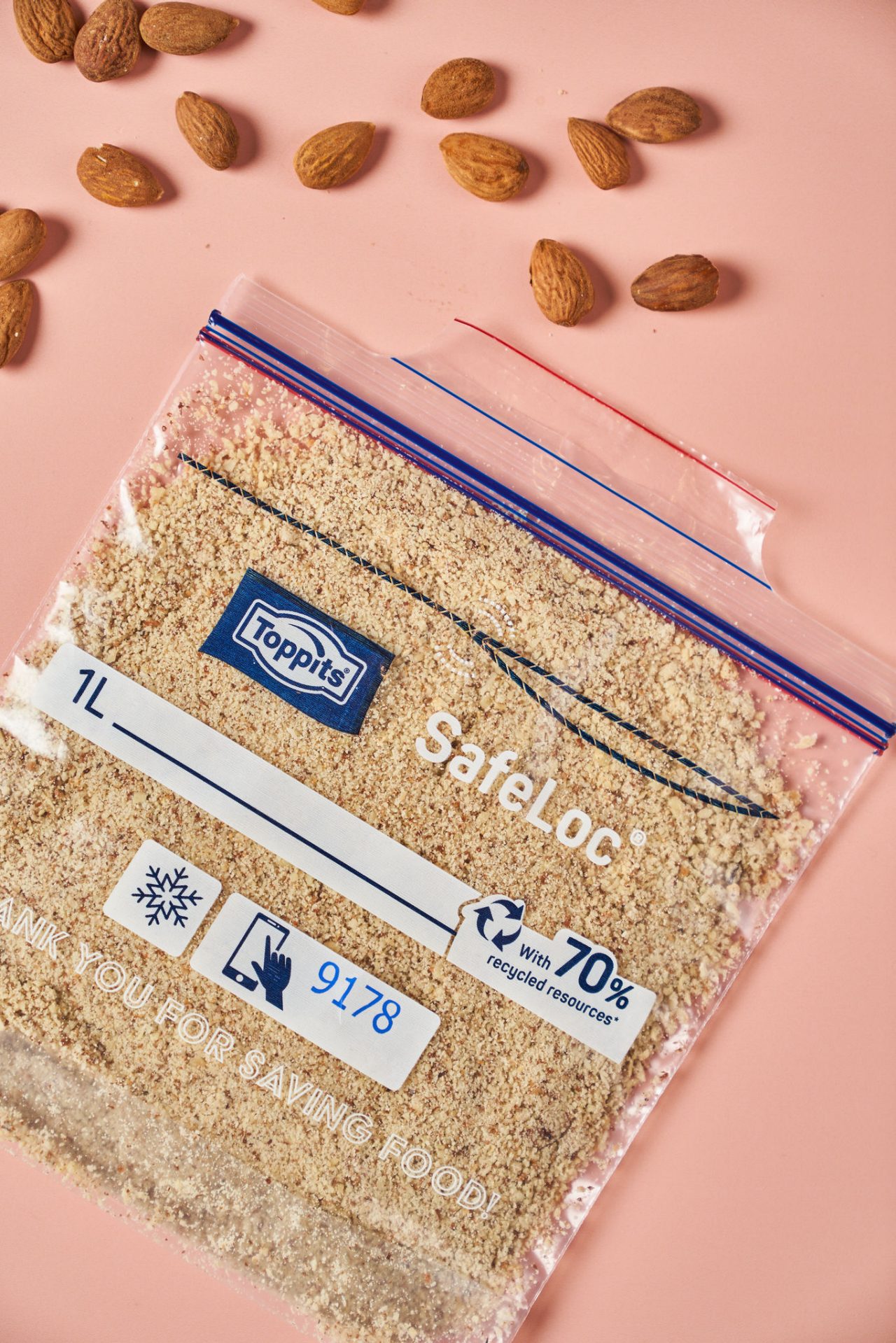 Gefrierbeutel von Toppits, gefüllt mit gemahlenen Mandeln, liegt auf einem rosa Untergrund. Daneben sind einige ganze Mandeln verteilt.