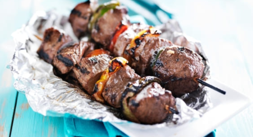 Gegrillte Fleischspieße mit Paprika und Zwiebeln liegen auf einem Teller, ausgelegt mit Toppits Alufolie. 