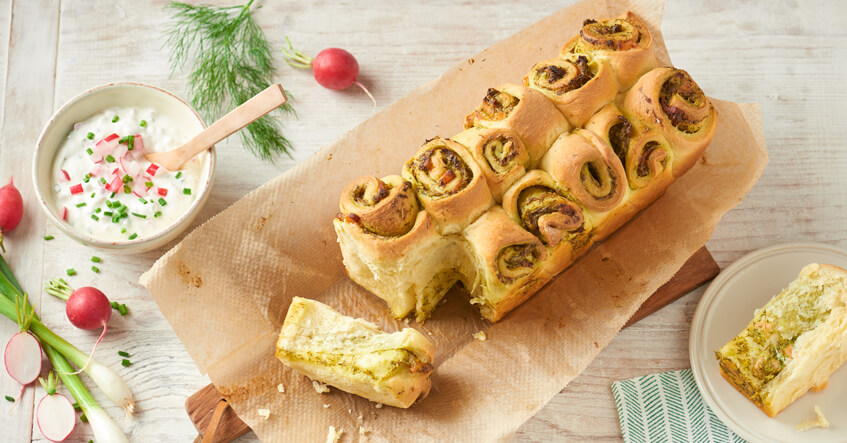 Pain en tranches sur du papier cuisson avec un bol de sauce aux herbes